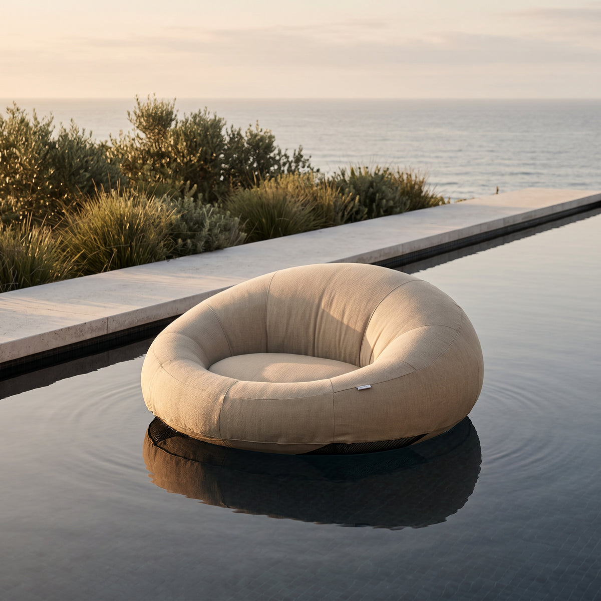 Poolboy Floata-Round in Natural floating on a coastal infinity pool at golden hour