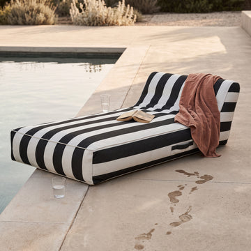 Poolboy Floata-Long in Black and White stripe by the pool, a towel left over it.