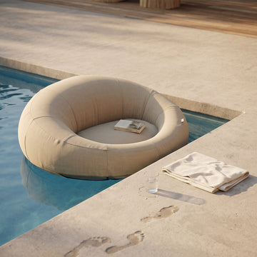 Poolboy Floata-Round in Natural beige at the pool edge, a book left on the seat.