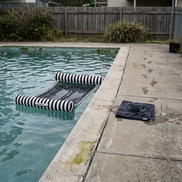 Poolboy Sinka-Bit in Black and White stripe in the pool, a towel left on the paving.
