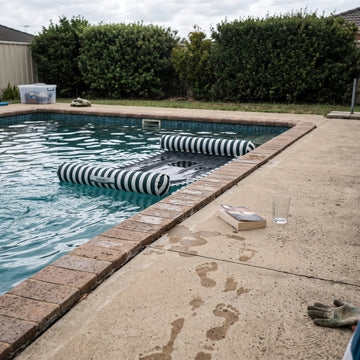Poolboy Sinka-Bit in Green and White stripe in the pool, a towel left on the paving.