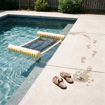 Poolboy Sinka-Bit in Yellow and White stripe in the pool, a towel left on the paving.